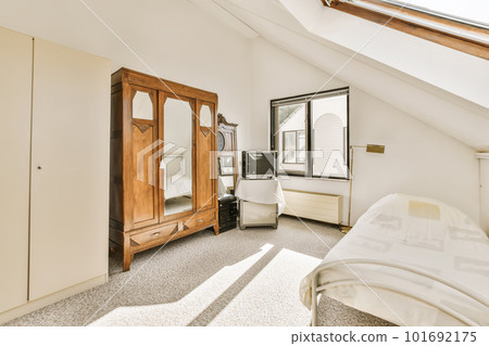 a bedroom with a bed, dresser and mirror in the corner of the room on the left is a window 101692175