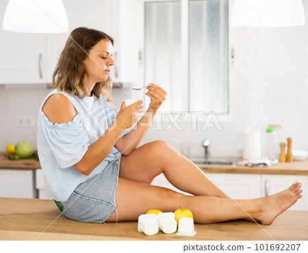 Young woman eating tasty yogurt in kitchen Young woman eating tasty yogurt in kitchen 101692207