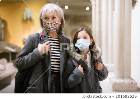 Elderly female tutor in protective mask showing tween girl ancient sculptures in museum Elderly female tutor in protective mask showing tween girl ancient sculptures in museum 101692629