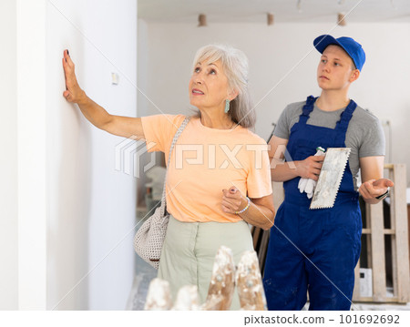 Mature woman checks the quality of plastered wall in room being renovated Mature woman checks the quality of plastered wall in room being renovated 101692692