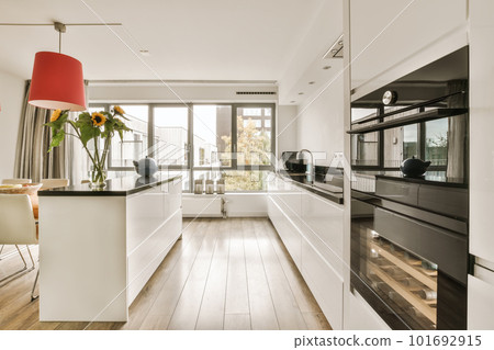 a modern kitchen with wood flooring and white cabinets in the center of the room is a red lamp hanging over the island 101692915