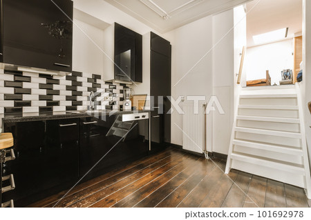 a kitchen with black and white tiles on the walls, wood flooring and stairs leading up to the upper level 101692978