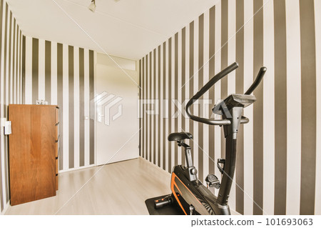 a gym room with an exercise bike on the floor and black and white striped wallpapers in the walls a gym room with an exercise bike on the floor and black and white striped wallpapers in the walls 101693063
