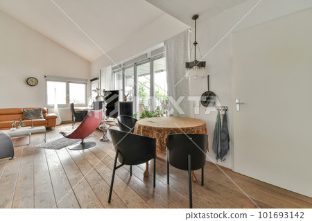 a living room with wood floors and white walls, including a round dining table surrounded by two black leather chairs 101693142