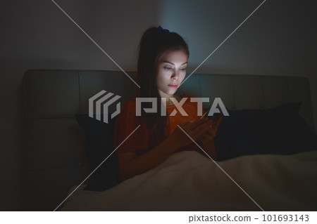 Woman sleeping using phone in bed staying up late at night reducing her sleep time which is bad for mental health and depression 101693143