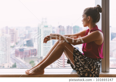 Mental health awareness in young women. Asian woman pensive looking out her condo window at home thinking about career choices, seasonal affective disorder in winter. Depression, loneliness Mental health awareness in young women. Asian woman pensive looking out her condo window at home thinking about career choices, seasonal affective disorder in winter. Depression, loneliness 101693147