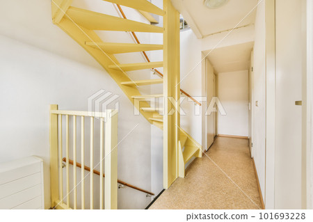 a hallway in an apartment with white walls and yellow staircase leading up to the second floor, there is a clock on the wall 101693228