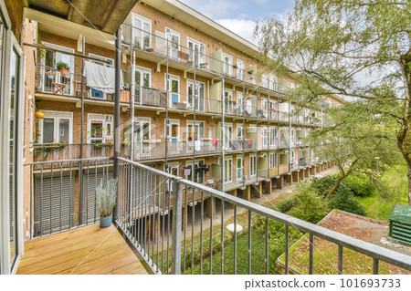 Amsterdam, Netherlands - 10 April, 2021: an apartment complex with balconys and balks on the second floor, trees in the fore - swayr Amsterdam, Netherlands - 10 April, 2021: an apartment complex with balconys and balks on the second floor, trees in the fore - swayr 101693733