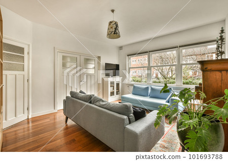 a living room with wood flooring and a blue couch in the center of the room is a large window a living room with wood flooring and a blue couch in the center of the room is a large window 101693788
