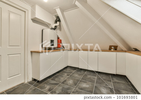 a small kitchen in a loft style space with tile flooring and white cupboards on either side, there is an open door a small kitchen in a loft style space with tile flooring and white cupboards on either side, there is an open door 101693801
