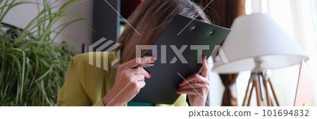 Tired and overworked woman covering face with clipboard 101694832
