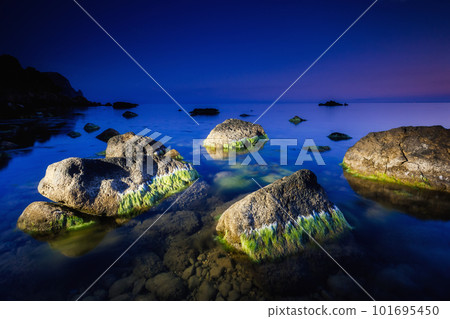 Large stones covered with algae are illuminated by a lantern in the dark sea. Large stones covered with algae are illuminated by a lantern in the dark sea. 101695450