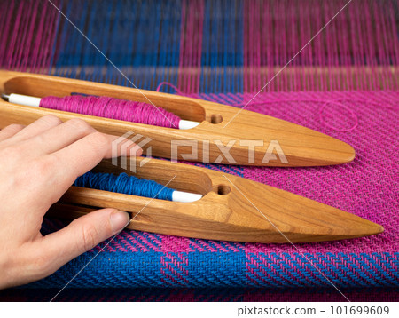 Hand takes a wooden boat shuttle with blue yarn to make a weaving project. Hand loom work Hand takes a wooden boat shuttle with blue yarn to make a weaving project. Hand loom work 101699609