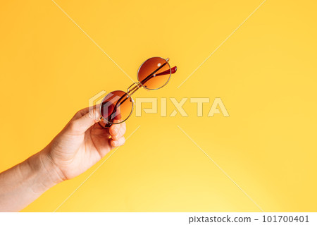 Round sunglasses in hand against yellow background Round sunglasses in hand against yellow background 101700401