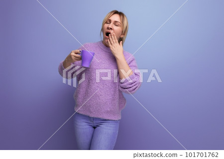 lovely blond young millennial woman in a casual look invigorates with a cup of coffee on a bright 101701762