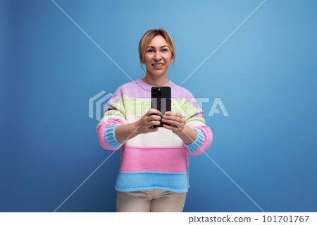 cute blond woman in a casual look takes a photo on a smartphone on a blue background 101701767