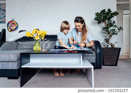 Mother and son drawing with color pencils and markers in the living room. Smiling mother has fun playing paint on paper with son on home family weekend, children creativity concept. Selective focus 101703257