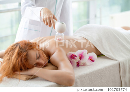 Woman getting anti-cellulite massage of back with use of vacuum cans in beauty studio Woman getting anti-cellulite massage of back with use of vacuum cans in beauty studio 101705774