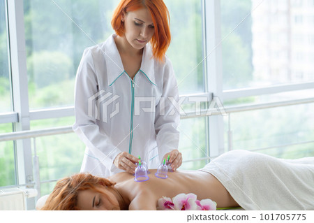 Woman getting anti-cellulite massage of back with use of vacuum cans in beauty studio Woman getting anti-cellulite massage of back with use of vacuum cans in beauty studio 101705775