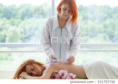 Woman getting anti-cellulite massage of back with use of vacuum cans in beauty studio Woman getting anti-cellulite massage of back with use of vacuum cans in beauty studio 101705780