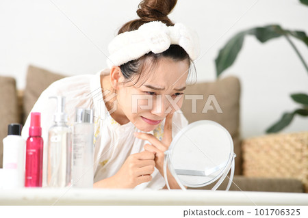 A woman suffering from skin problems while looking in the mirror A woman suffering from skin problems while looking in the mirror 101706325
