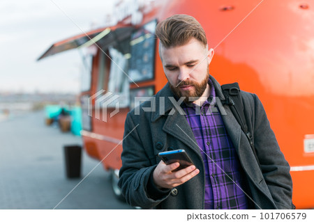 Portrait of handsome young man with smartphone standing in front of food truck - food delivery and restaurant app Portrait of handsome young man with smartphone standing in front of food truck - food delivery and restaurant app 101706579