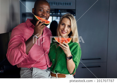 Multiracial couple eating melon in kitchen during hot sunny days. 101707787