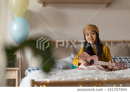 Happy girl playing on the guitar in her room. 101707804