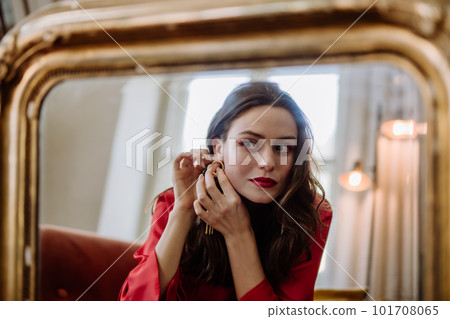 Young woman in elegant dress preparing for evening, looking in a mirror. 101708065