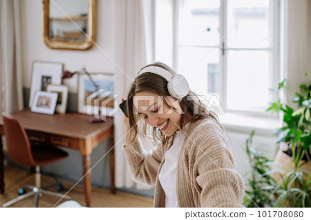 Young woman listening music trough headphones in her apartment. Young woman listening music trough headphones in her apartment. 101708080