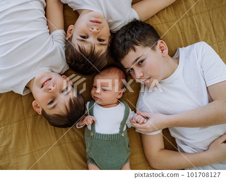 Three big brothers with their little newborn brother lying in bed. 101708127