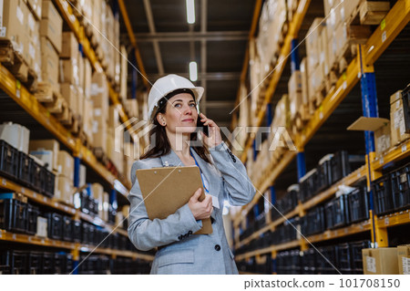 Manager woman in suit calling in a waehouse. 101708150