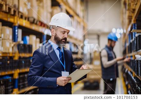 Manager in suit controlling goods in a warehouse. 101708153