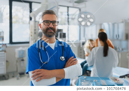 Portrait of mature doctor in surgery room, mother with child in background. 101708476