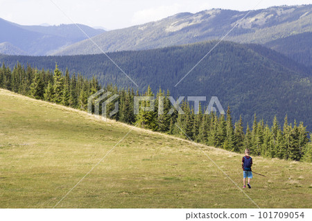 Young happy child boy with backpack walking in mountain grassy valley on background of summer woody mountain. Active lifestyle, adventure and weekend activity concept. Young happy child boy with backpack walking in mountain grassy valley on background of summer woody mountain. Active lifestyle, adventure and weekend activity concept. 101709054