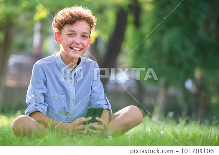 Young boy browsing his smartphone outdoors in summer park. Using cellphone for leasure and education concept 101709106