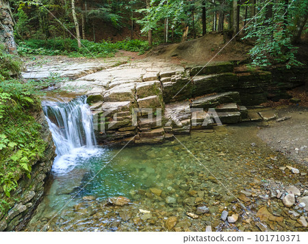 Waterfall on mountain river with white foamy water falling down from rocky formation in summer forest. 101710371