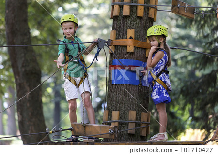 Two children, boy and girl in protective harness and safety helmets at climbing activity on rope way. 101710427