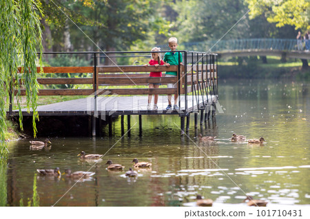 Two children boy and girl standing on wooden deck on a lake shore feeding ducks Two children boy and girl standing on wooden deck on a lake shore feeding ducks 101710431