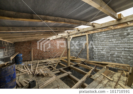 Spacious attic room under construction and renovation. Energy saving walls of large hollow foam insulation blocks and temporary wooden scaffolding, long logs as roof frame. Construction, masonry. Spacious attic room under construction and renovation. Energy saving walls of large hollow foam insulation blocks and temporary wooden scaffolding, long logs as roof frame. Construction, masonry. 101710591