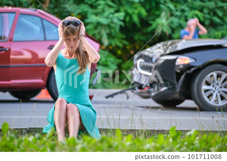Sad female driver sitting on street side shocked after car accident. Road safety and vehicle insurance concept. Sad female driver sitting on street side shocked after car accident. Road safety and vehicle insurance concept. 101711008