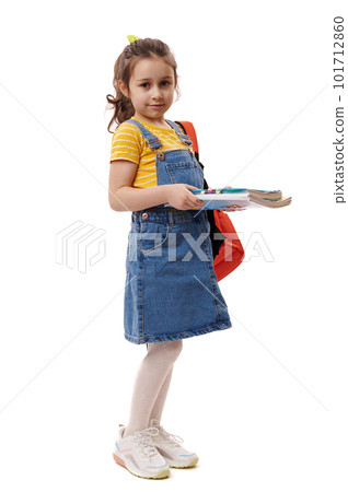 Full length portrait of Caucasian smiling excellent best student, first grader schoolgirl, 5-6 years old little girl holding books and copybooks going to school, isolated on white background. Ad space 101712860