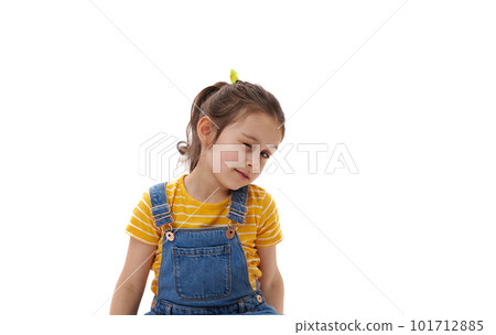Close-up vertical emotional portrait of Caucasian lovely baby girl in bright yellow t-shirt and blue denim overalls, blinking, winking looking at camera, isolated over white background. Copy ad space Close-up vertical emotional portrait of Caucasian lovely baby girl in bright yellow t-shirt and blue denim overalls, blinking, winking looking at camera, isolated over white background. Copy ad space 101712885