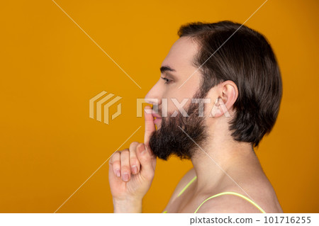 Side view of bearded transsexual person holding finger near lips making silence gesture keeps secret Side view of bearded transsexual person holding finger near lips making silence gesture keeps secret 101716255