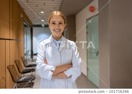 Friendly young blonde female doctor standing in hospital corridor, nurse wearing lab coat. Friendly young blonde female doctor standing in hospital corridor, nurse wearing lab coat. 101716266