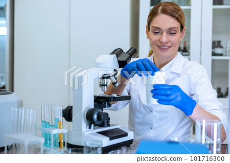 Female scientist in lab coat and gloves using microscope microbiologist working in modern laboratory 101716300