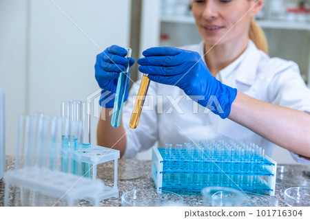 Woman biologist holds test tubes with yellow and blue liquids in hands doing experiments in biology 101716304