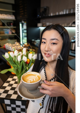 Smiling coffeehouse visitor with a caffeinated drink in her hand 101716496
