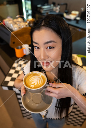 Contented cafe visitor holding a caffeinated beverage in her hand 101716497