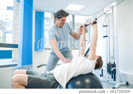 Male patient having a session of rehabilitation exercises on a fitball 101716504